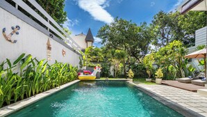 Une piscine avec un jouet flottant, entourée de verdure et bordée d’un mur blanc agrémenté d’éléments décoratifs.