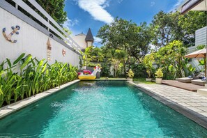A swimming pool with a floating toy, surrounded by greenery and a white wall with decorative elements. - Villa Avaluna (by JB Villas) (Legian)