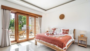 Une chambre avec un grand lit, une table de chevet en bois, une porte-fenêtre coulissante donnant sur un espace extérieur et un luminaire fixé au plafond.