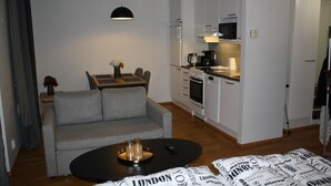 Ett kompakt vardagsrum med en grå soffa, ett litet matbord och en liten köksdel.