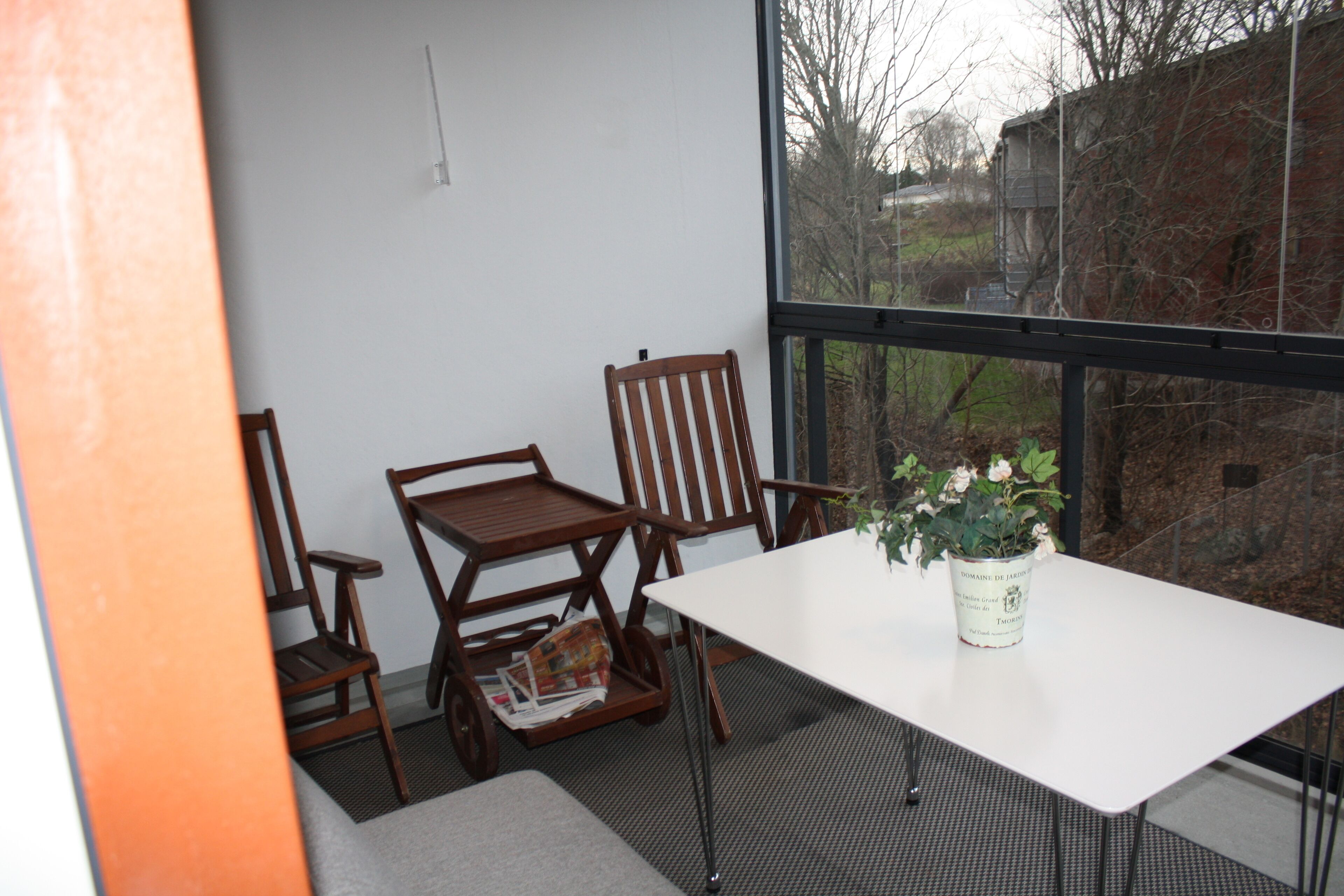 Ein Zimmer mit einem weißen Tisch, zwei Holzsesseln, einem kleinen Tisch mit einer Zeitung und einer Topfpflanze.