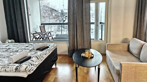 Ett hotellrum med en säng, en soffa, ett litet bord med ett bricka på och utsikt över ett snötäckt landskap genom stora fönster.