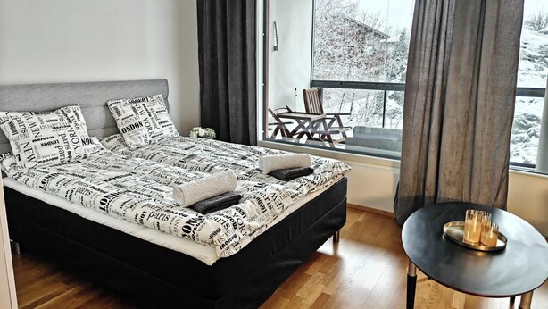 Ett modernt sovrum med en stor säng, ett litet bord med glas och utsikt över ett snötäckt landskap genom ett fönster.