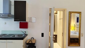 A compact kitchen with a stove, sink, and cabinets, leading to a bedroom with a bed and a large mirror. - Superior Studio for 3 in Konstanz (Konstanz)