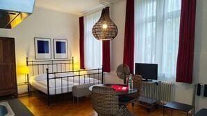 A hotel room with a bed, a desk with a chair, a television, a radiator, and a window with curtains. - Superior Studio for 3 in Konstanz (Konstanz)