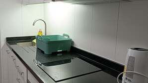 Una cocina moderna con armarios blancos, encimera negra, horno empotrado y cafetera.
