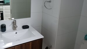 Un baño con un lavamanos blanco, tocador de madera, un espejo, ducha y un inodoro.
