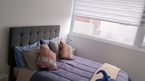 Un dormitorio con cama, almohadas, una ventana con persianas y una lámpara de techo.