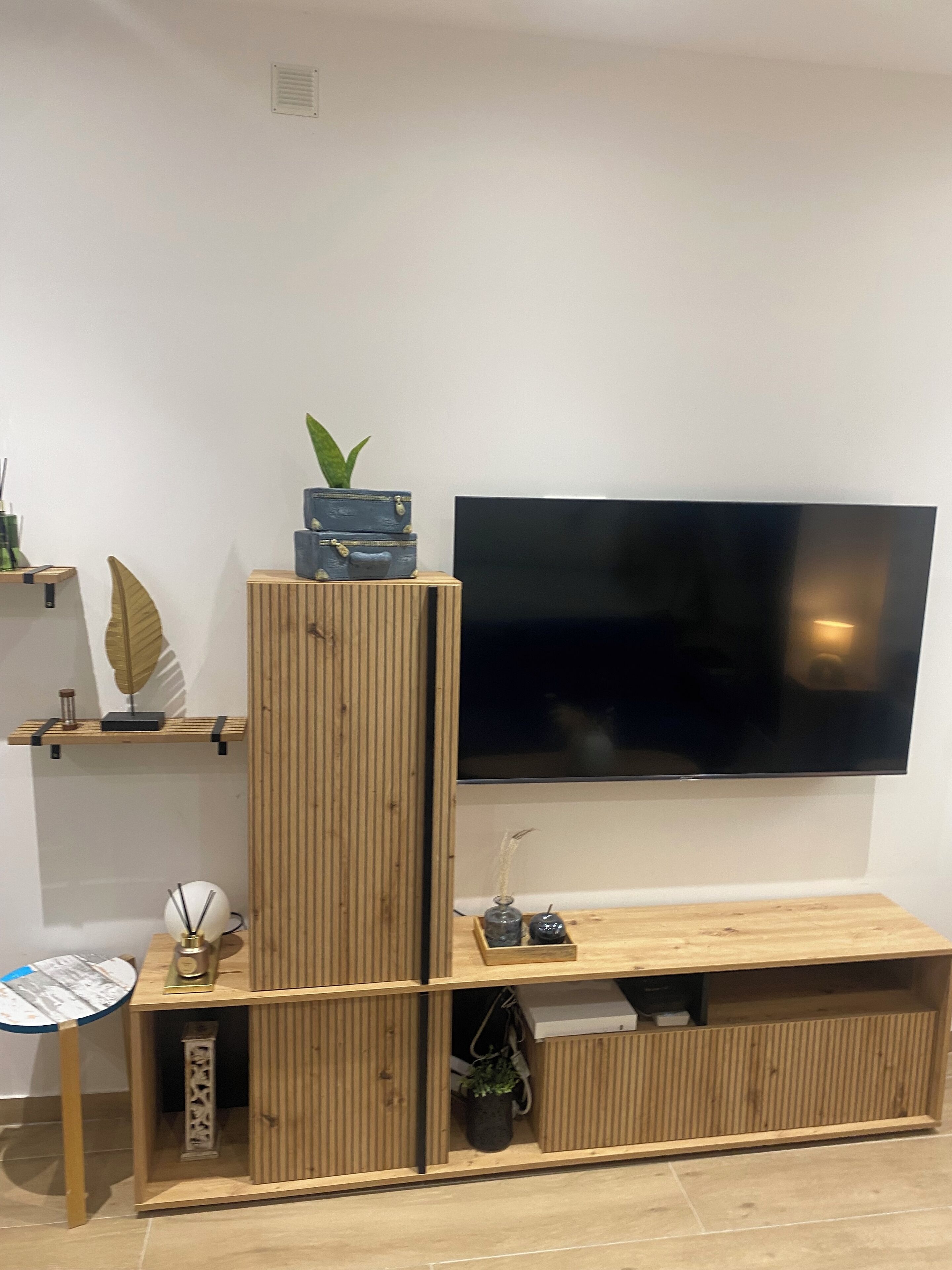 Ett modernt vardagsrum med en platt-TV som är monterad på väggen, möbler i trä och dekorativa föremål, inklusive växter och en jordglob.