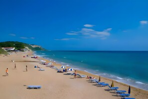 Une plage avec des transats et des parasols, un ciel dégagé et une côte.