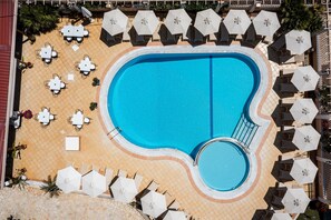 Une grande piscine à bords incurvés, entourée de chaises longues et de parasols.