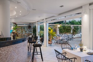 A restaurant with a bar area, outdoor seating, and a view of greenery. - Metaxa One-Bedroom 6 Apartment with Shared Pool, Wi-Fi, and Air Conditioning (Κάβος)