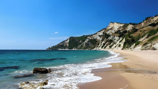 Una spiaggia con acque cristalline, una riva sabbiosa e scogliere rocciose.