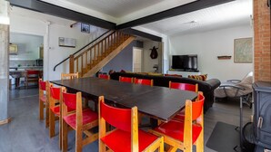 A dining area with a long table and red chairs, a staircase, a television, and a fireplace. - Gîte Crèmouille – In the Heart of the Vercors Regional Natural Park (Saint-Agnan en Vercors)