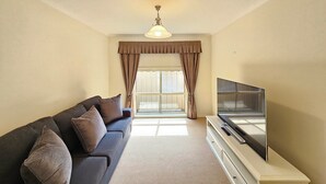 A living room with a sofa, a TV on a stand, and a window with curtains. - Flipping Flounder - Coastal Comfort in Robe’s Heart (Robe)