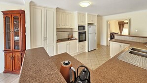 A kitchen with white cabinets, a microwave, a refrigerator, and a wooden cabinet with glass doors. - Flipping Flounder - Coastal Comfort in Robe’s Heart (Robe)