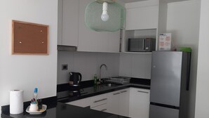 A modern kitchen with a central island, white cabinetry, a stainless steel refrigerator, a microwave, and a green pendant light. - Kasa and family 220 (Valdivia)