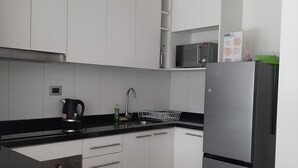 A modern kitchen with white cabinets, a black countertop, a stainless steel refrigerator, and a microwave. - Kasa and family 220 (Valdivia)