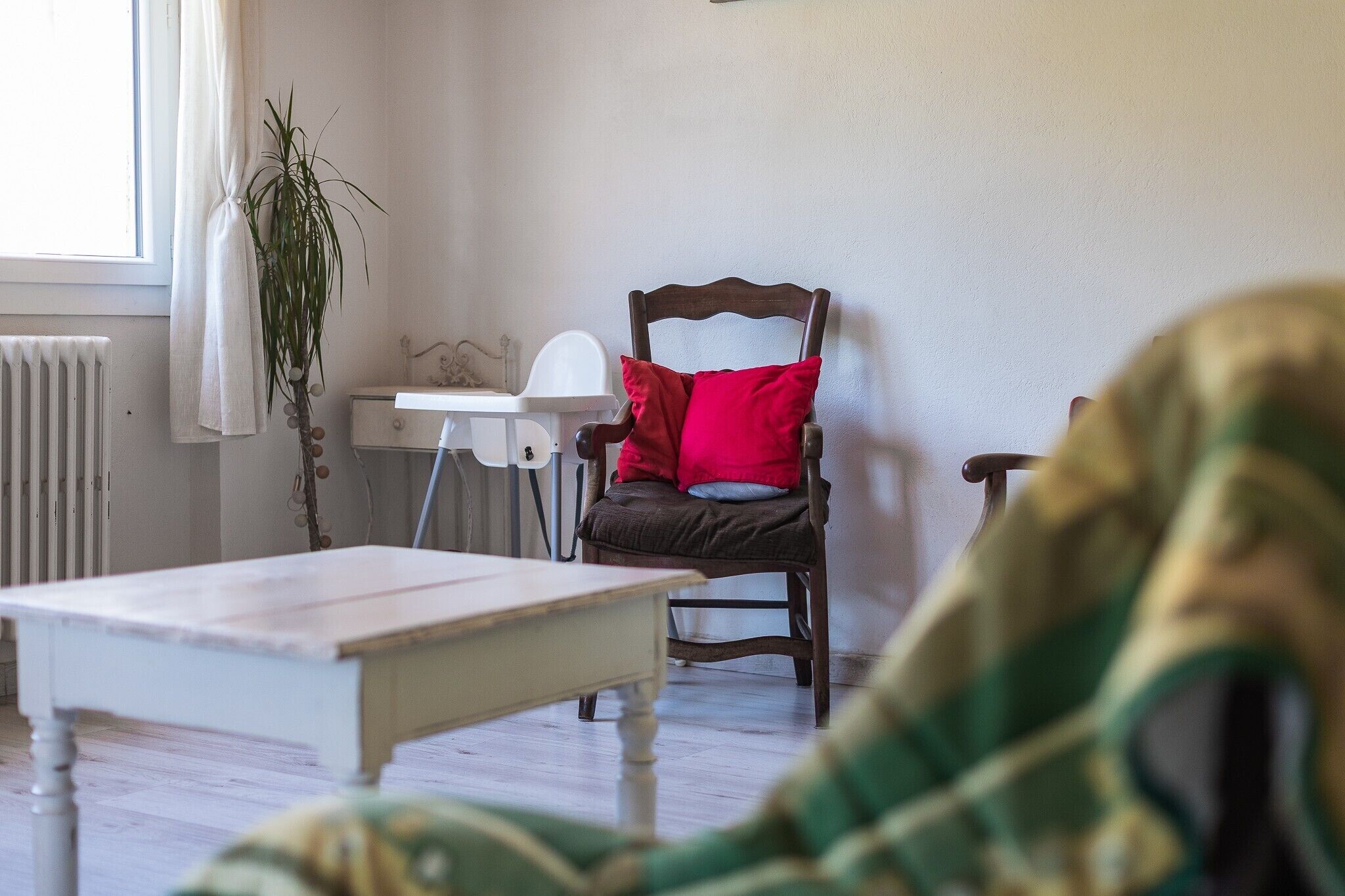 Ein Zimmer mit einem Holzbett, einem weißen Tisch, einem Heizkörper und einem Fenster mit Vorhängen.