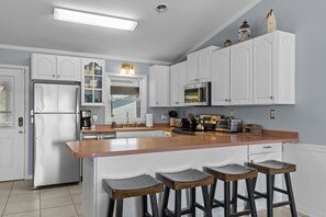 A kitchen with white cabinetry, a stainless steel refrigerator, a microwave, and a wooden island with bar stools. - Morning Mist | Ocean Views, Near Beach, Screened Porch (Emerald Isle)