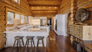 Cuina d'una cabana de fusta amb una illa central, tamborets de fusta i un armari metàl·lic amb calaixos.
