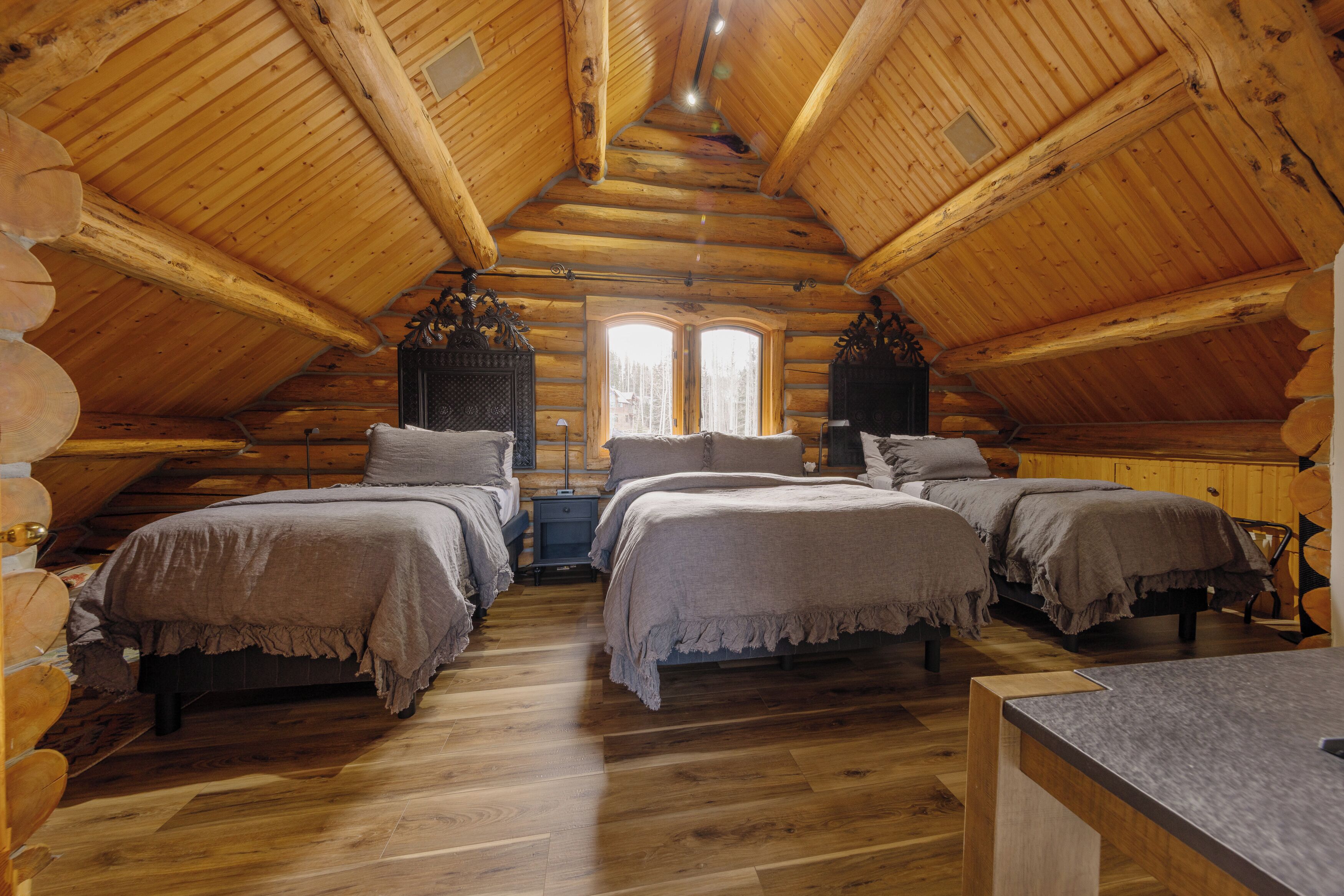 A log cabin bedroom with three beds, wooden floors, and a sloped ceiling.