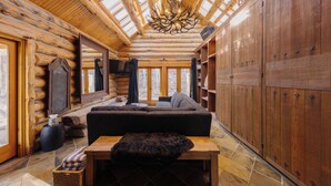 Interior d'una cabana de fusta amb sostre de fusta, un penjall, un sofà i una llar de foc.
