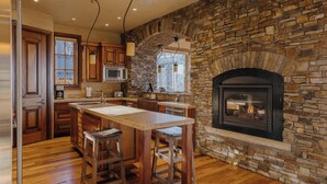 Una cocina con chimenea de piedra, armarios de madera y una isla central con taburetes.