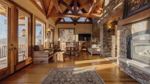 Amplia sala de estar con pisos de madera, chimenea de piedra y ventanas grandes que permiten la entrada de luz natural.