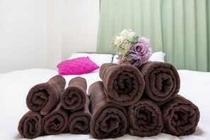 Ein ordentlich gemachtes Bett mit aufgerollten braunen Handtüchern und einem Blumenstrauß.