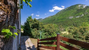 Une porte en bois donnant sur un sentier, entourée d’une végétation luxuriante et avec une chaîne de montagnes en arrière-plan.