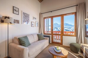 A living room with a sofa, a coffee table, and a view of a snowy landscape through a balcony door. - Thémi 522 - Thémis 522 - Le Alti Nid - Luxury Belle-Plagne (La Plagne Tarentaise)