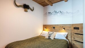 Ein Schlafzimmer mit Holz-Kopfteil, einem Wandbild von einer Berglandschaft, einem Bett mit einer grün gemusterten Decke und einem aufgehängten Geweih.