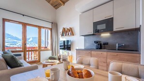 Eine moderne Küche mit großem Fenster, ein Essbereich mit gedecktem Tisch für das Frühstück und ein gemütlicher Wohnbereich mit einer Couch.