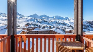Ein Holzbalkon mit Blick auf schneebedeckte Berge und eine Berghütte.