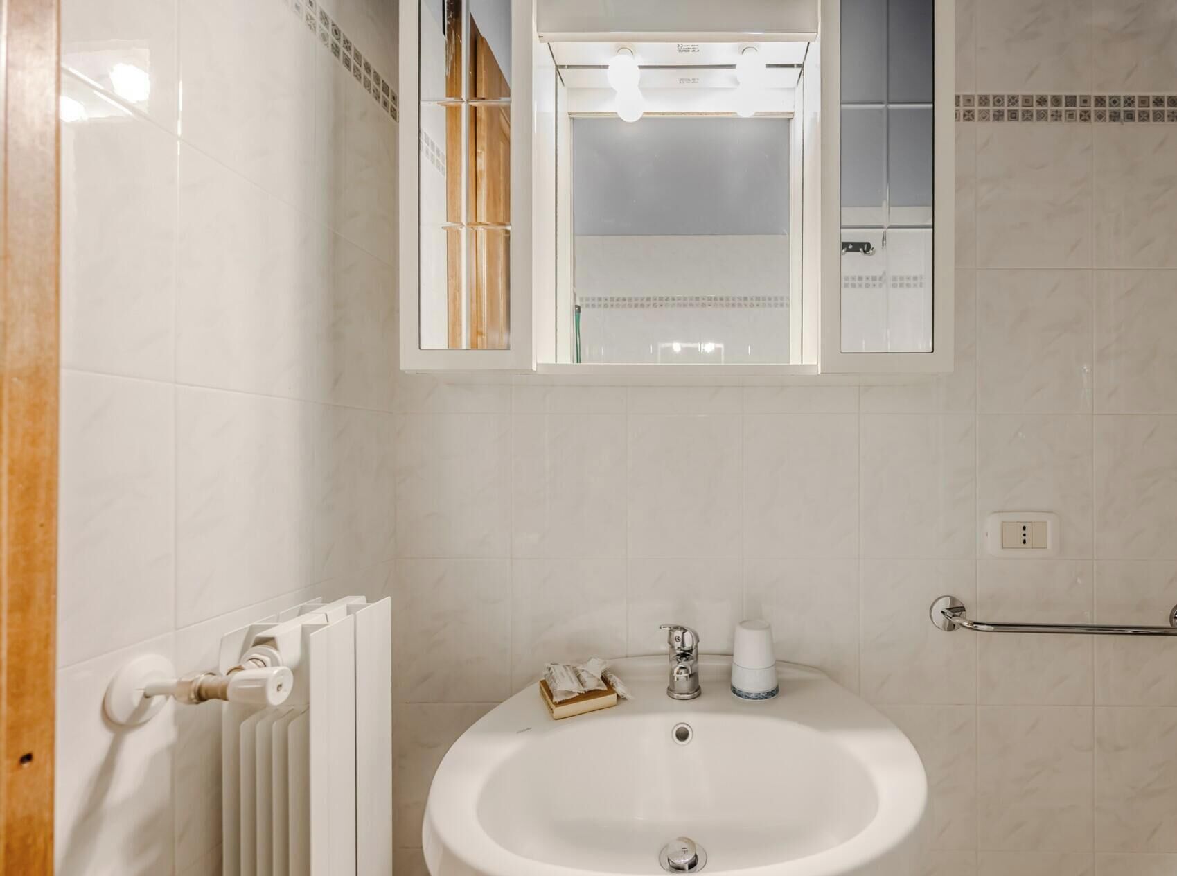 A bathroom with a white sink, a mirror, a towel rack, and a radiator.