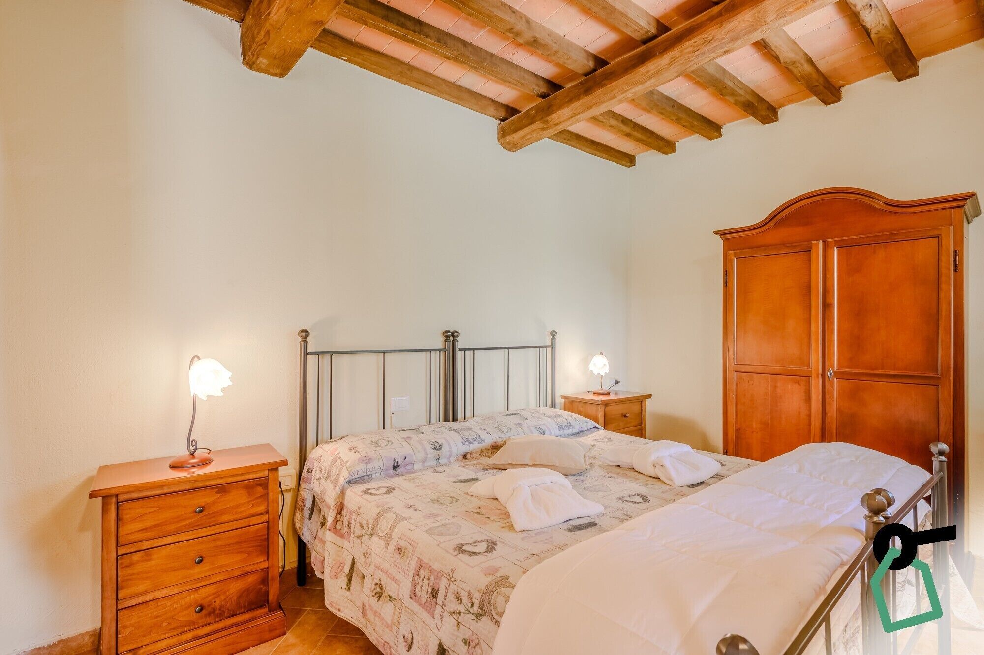 Una camera da letto con un letto, comodini in legno, un armadio e un soffitto con travi a vista.