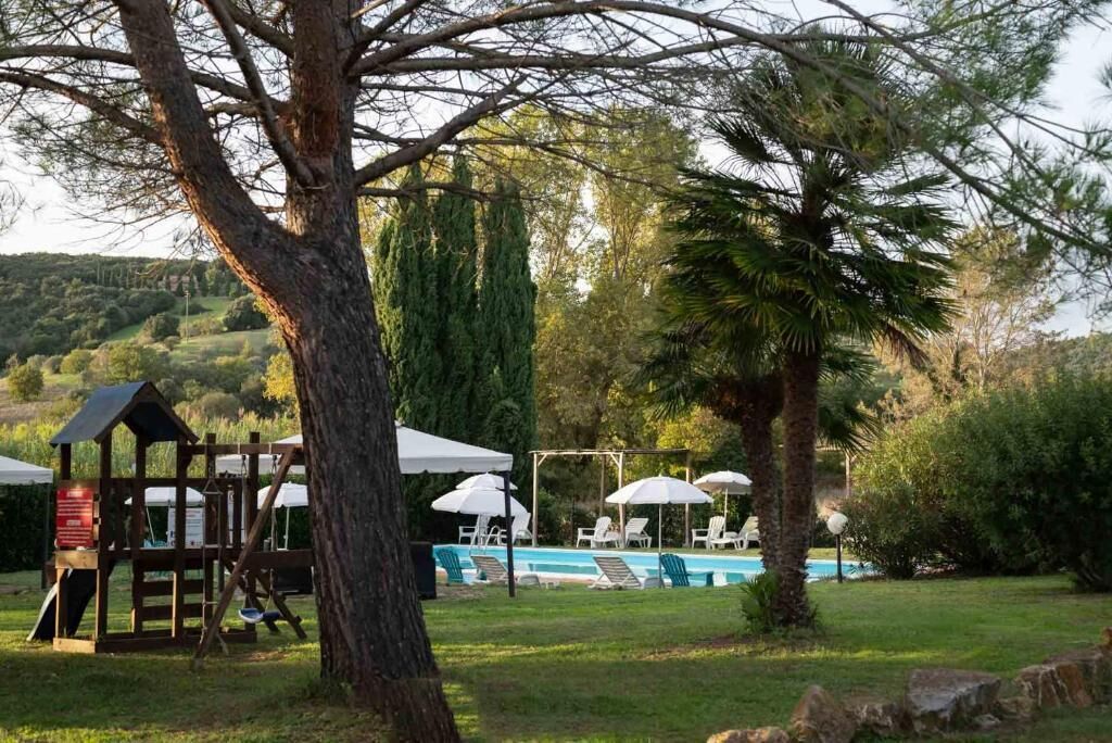 A pool area with lounge chairs and umbrellas, surrounded by trees and a wooden structure.