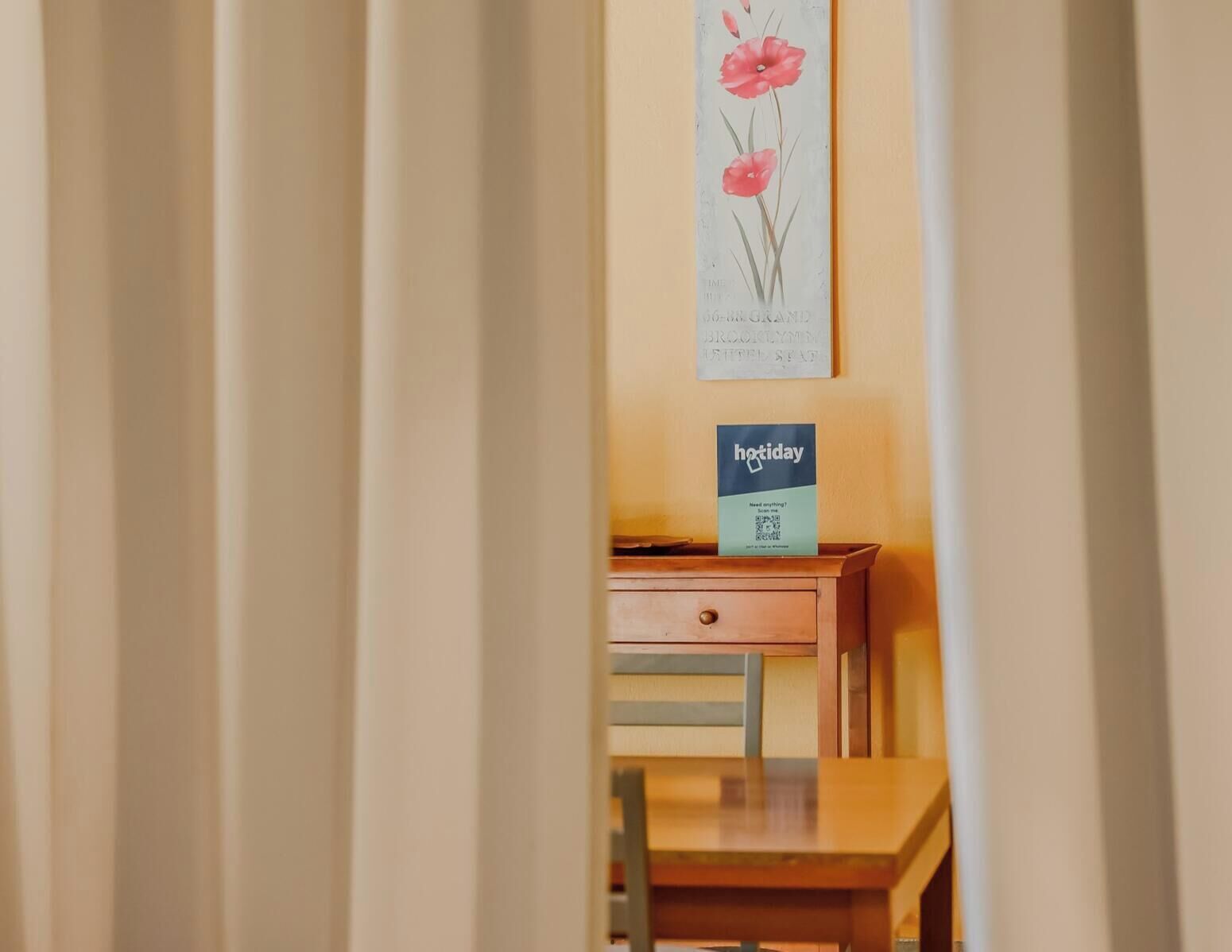 A hotel room with a wooden desk, a framed botanical illustration on the wall, and a 'holiday' sign on the desk.