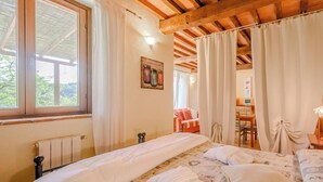 Ein Schlafzimmer mit einem großen Bett, Holzbalkendecke, Heizkörper und einem Vorhangfenster.