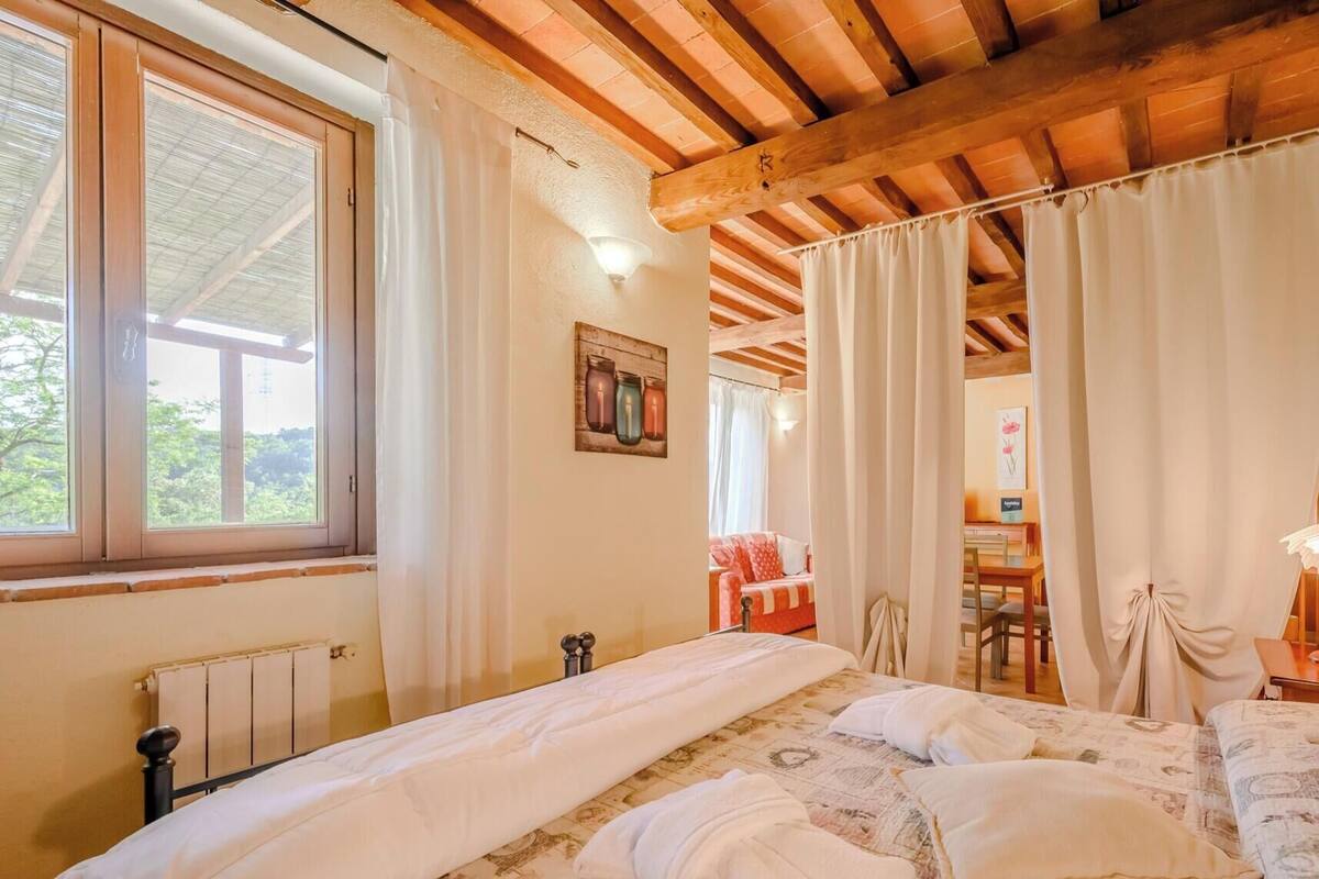 A bedroom with a large bed, wooden ceiling beams, a radiator, and a window with curtains.