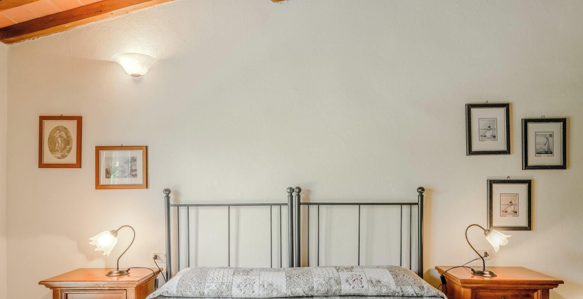 A bedroom with a metal bed frame, two bedside tables with lamps, and framed pictures on the walls.