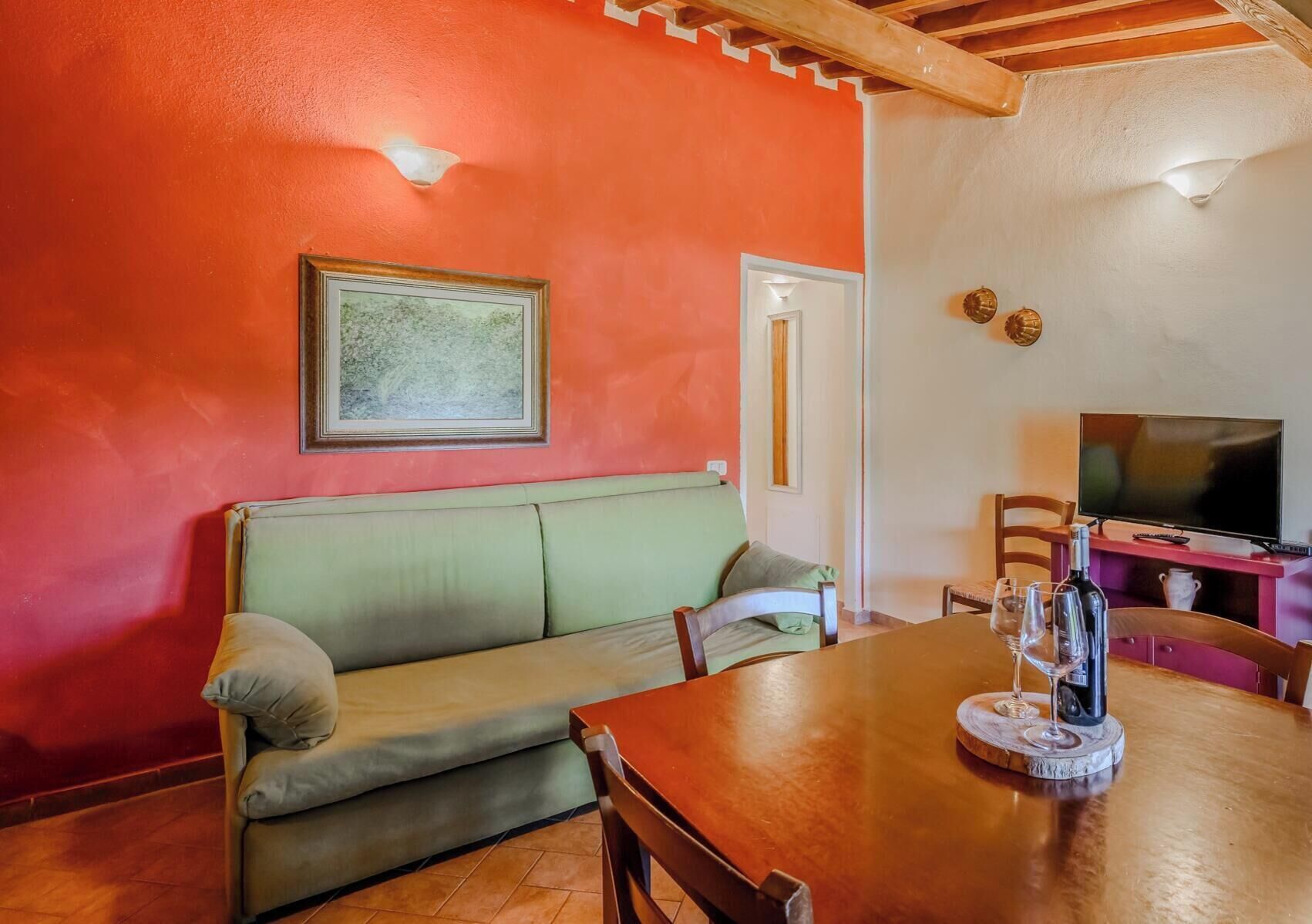 Una habitación con una mesa de comedor de madera, un sofá verde, un televisor y un cuadro en la pared.