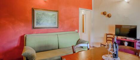 Una habitación con una mesa de comedor de madera, un sofá verde, un televisor y un cuadro en la pared.