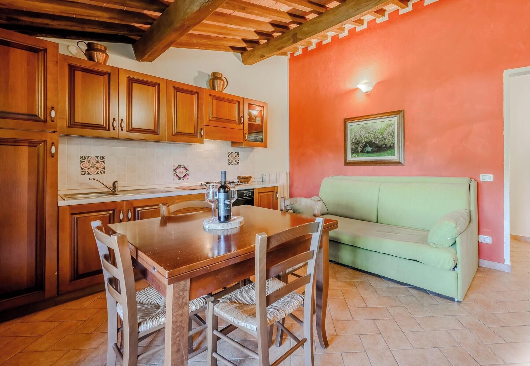 A kitchen with wooden cabinets, a dining table with chairs, a green sofa, and a tiled floor.