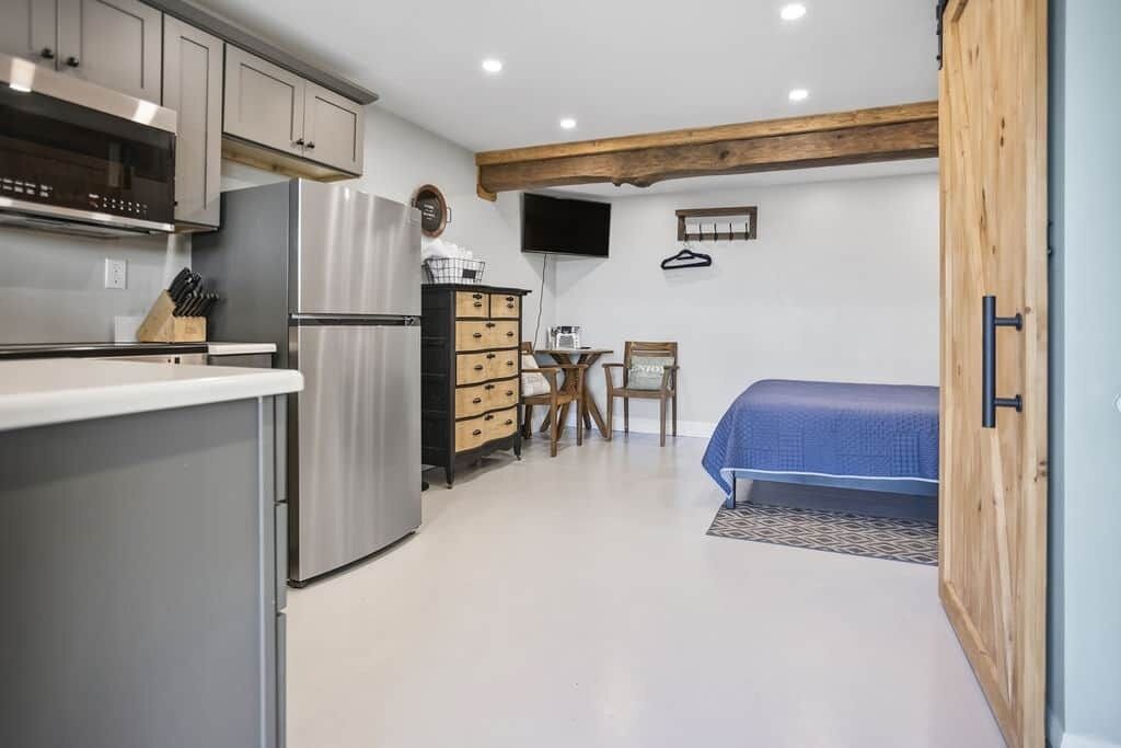 Cocina compacta con electrodomésticos modernos, comedor con mesa y sillas, y una cama en la habitación contigua.