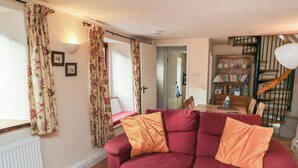 Una sala de estar con un sofá rojo, cortinas con motivos florales, piso de madera y una escalera al fondo.