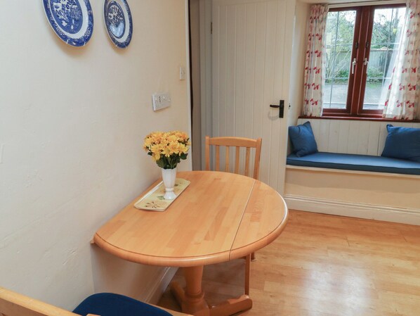 A dining area with a wooden table, a vase of flowers, and a bench with blue cushions.