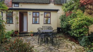 Un pintoresco cottage con techo de paja, patio de piedra y un pequeño jardín.