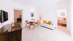 Un soggiorno moderno con TV a schermo piatto, un tavolo da pranzo con sedie, un divano bianco con cuscini gialli e un bagno con specchio e lavandino.